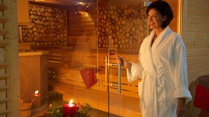 Un sauna aux murs en bois, avec une porte en verre et une bougie rouge posée sur le sol.
