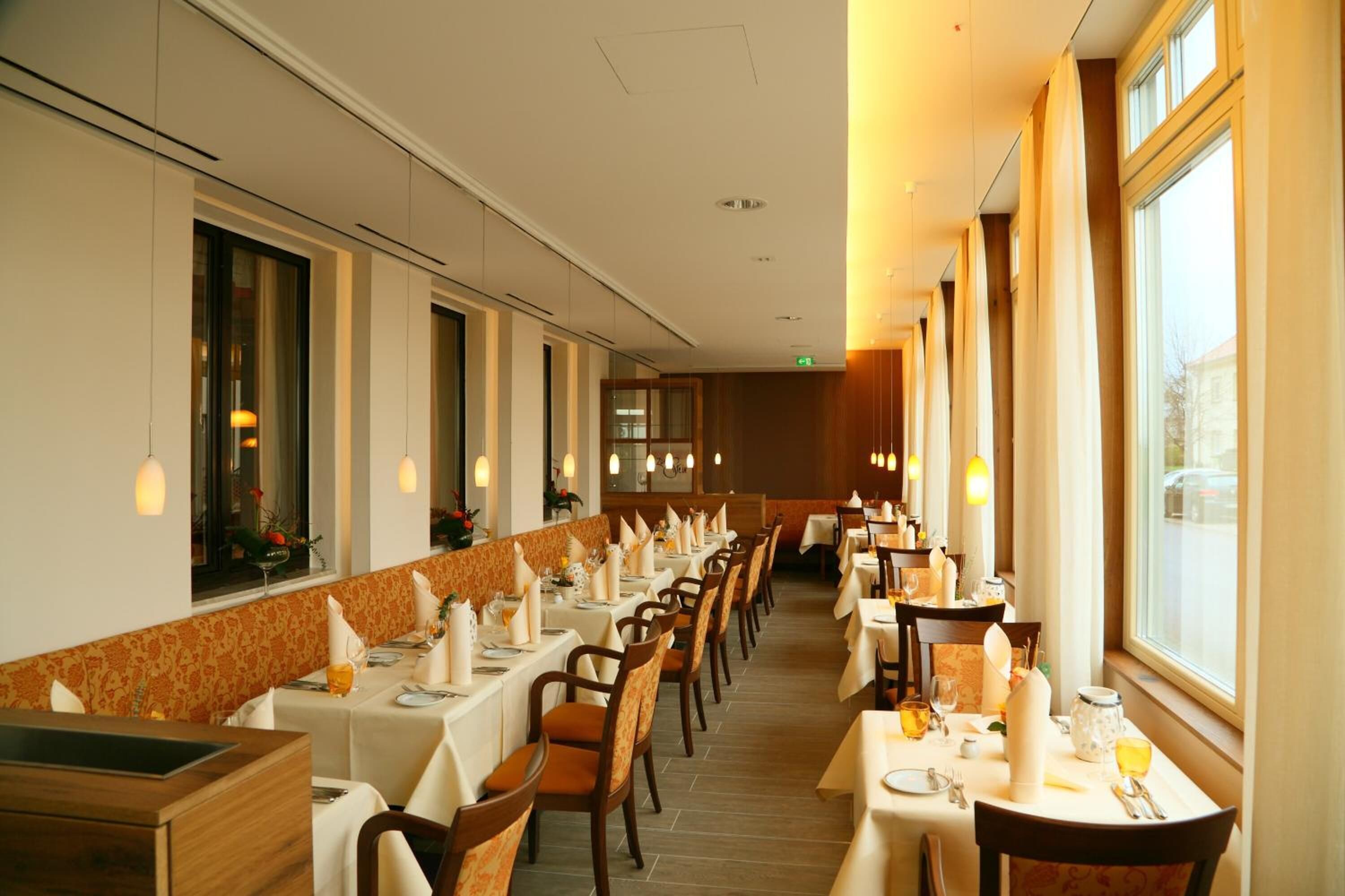 A restaurant with long tables and chairs, a patterned wall, and large windows.