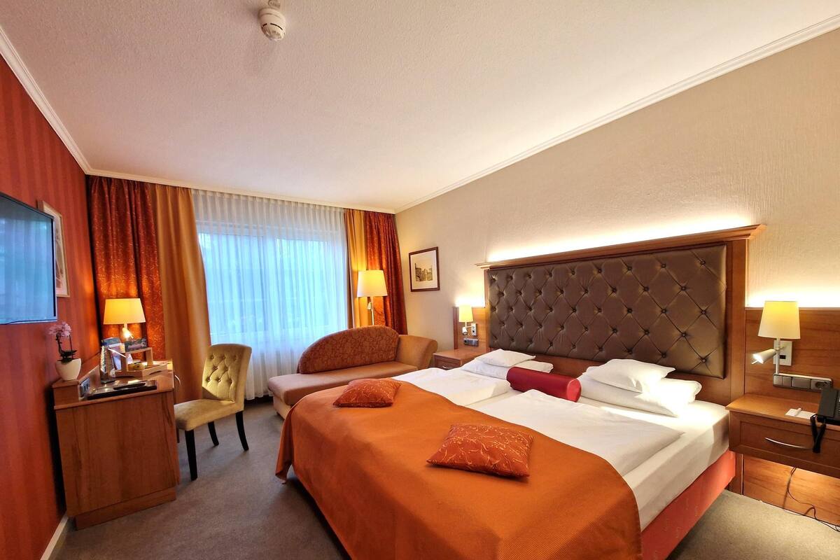 A hotel room with a large bed, two bedside tables, a chair, a desk, and a television.