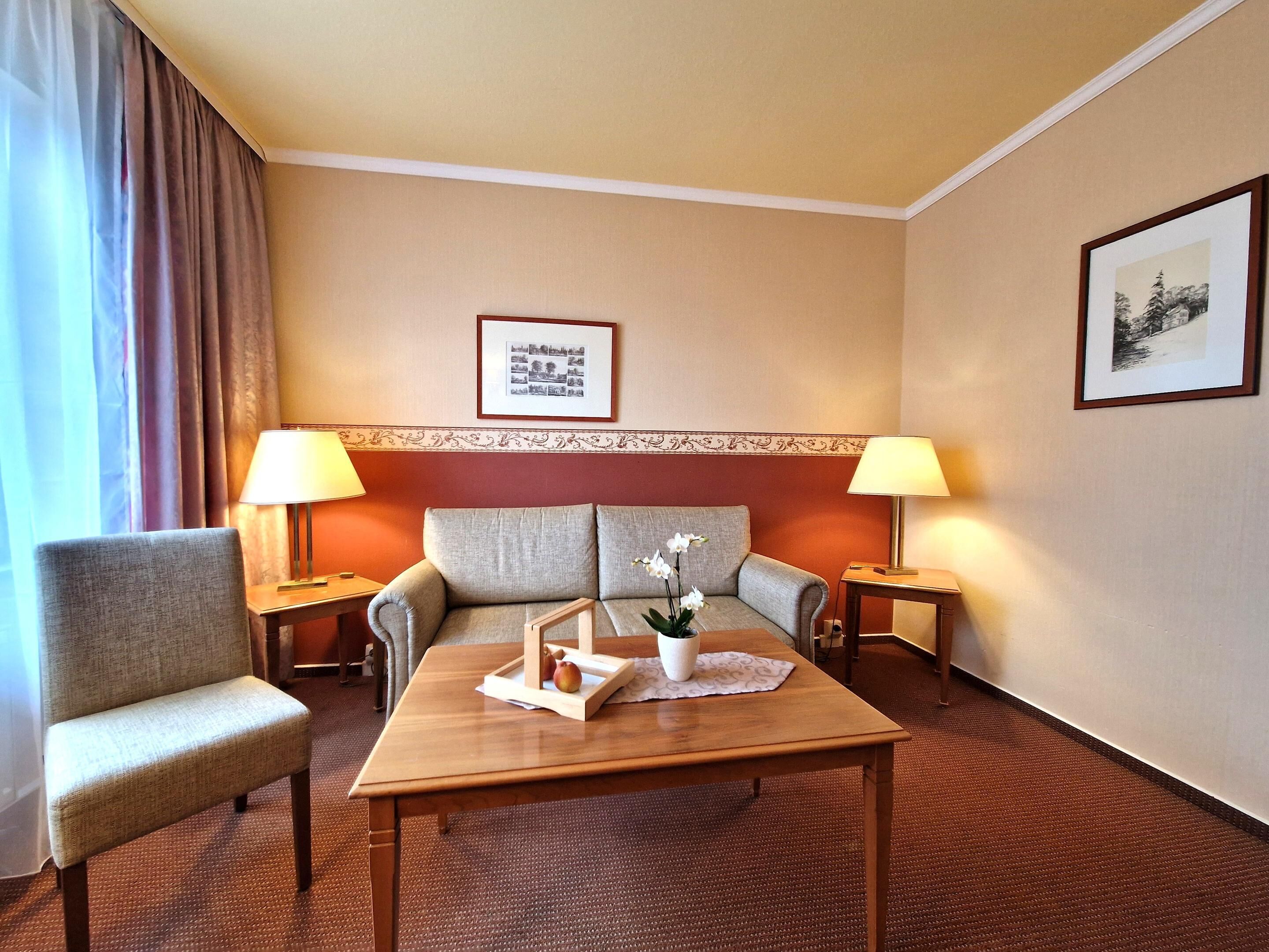 A hotel room with a sofa, two armchairs, a wooden coffee table, and two bedside lamps.
