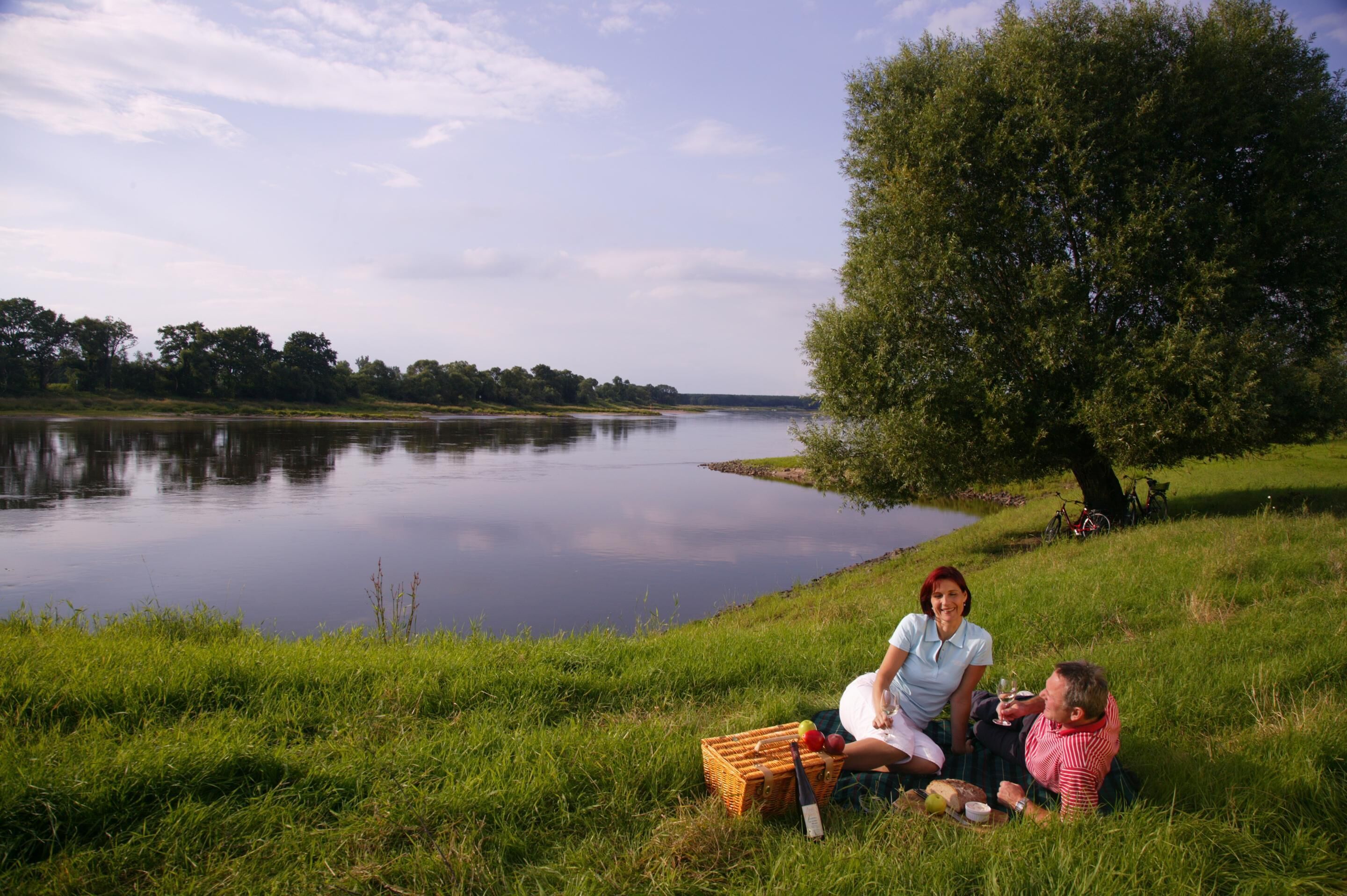 A lakeside picnic with a picnic basket, a bottle, and a blanket.