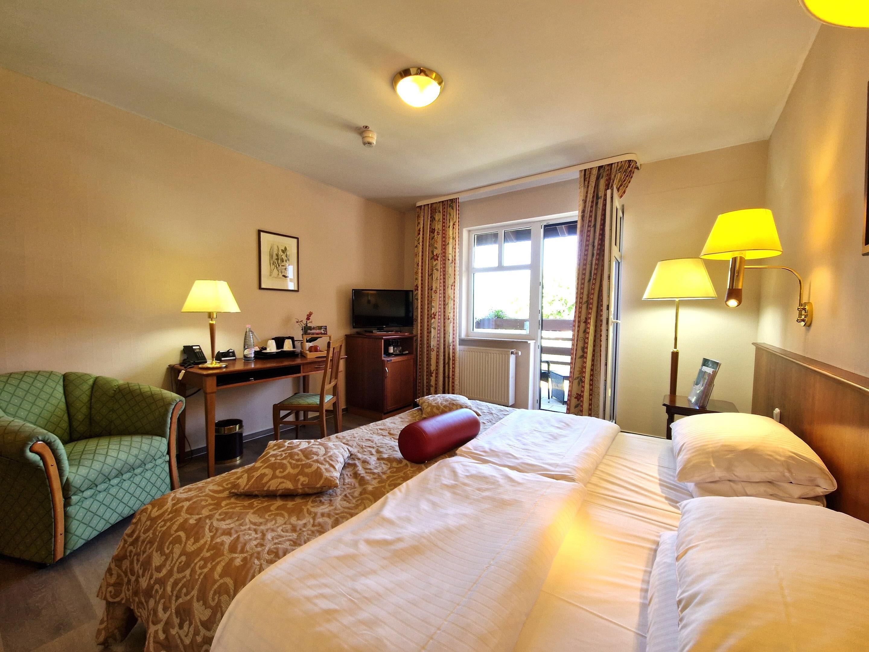 Une chambre d’hôtel avec deux lits, un bureau avec une télévision, une chaise et une fenêtre avec des rideaux.