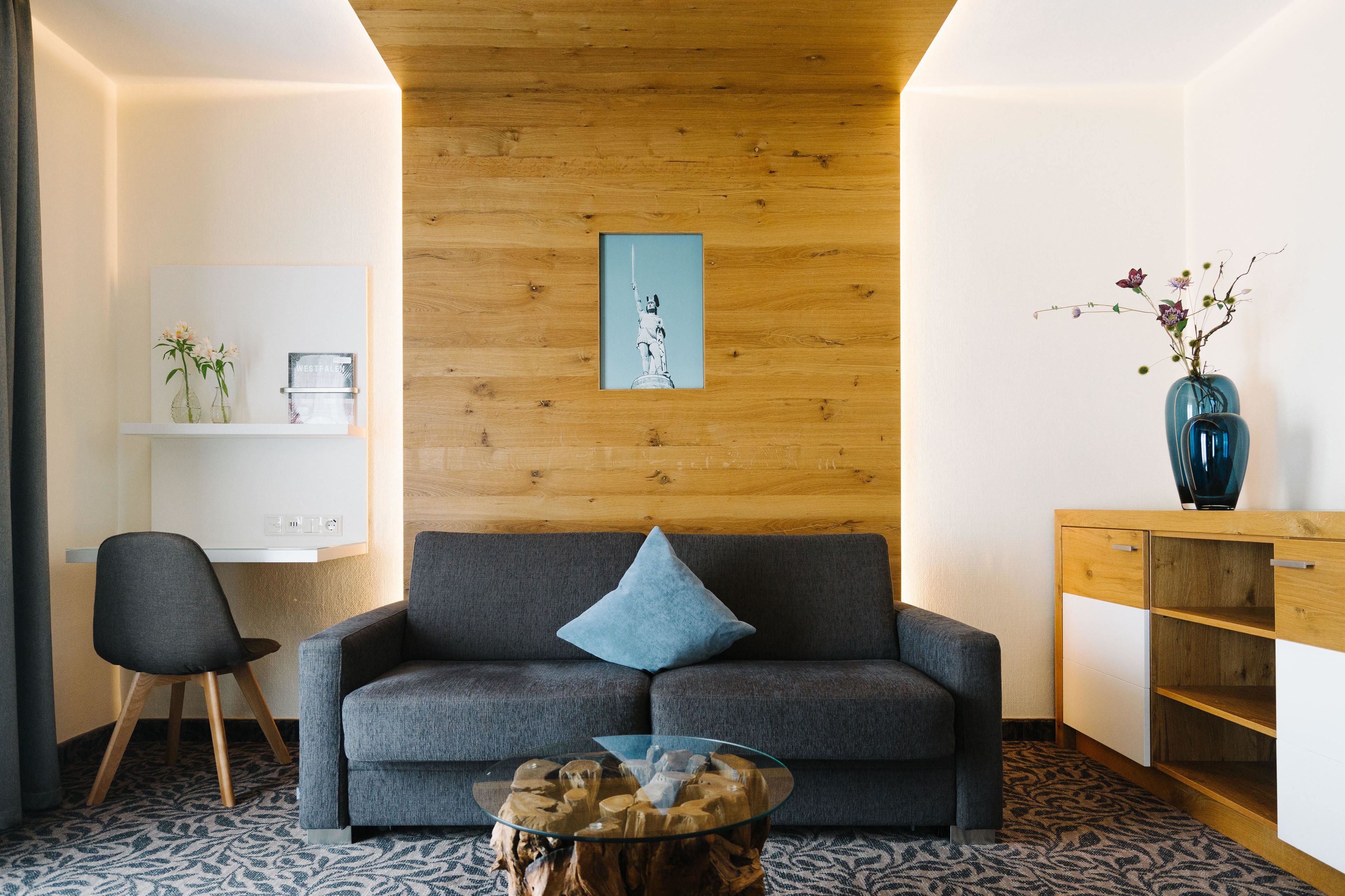 A modern living room with a grey sofa, a glass coffee table, a wooden cabinet, and a wall-mounted shelf with decorative items.