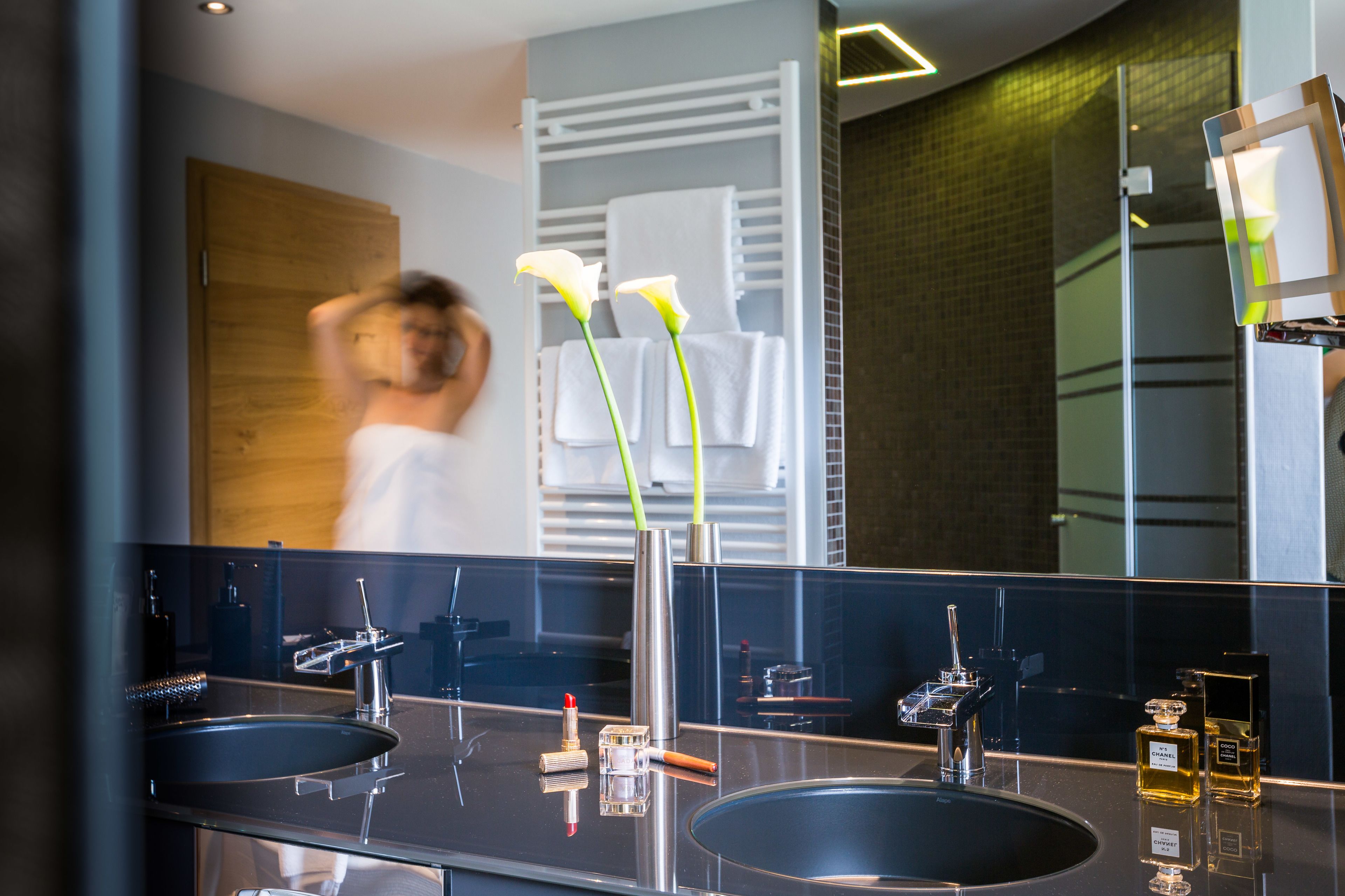 A modern bathroom with two sinks, a large mirror, and a towel rack.