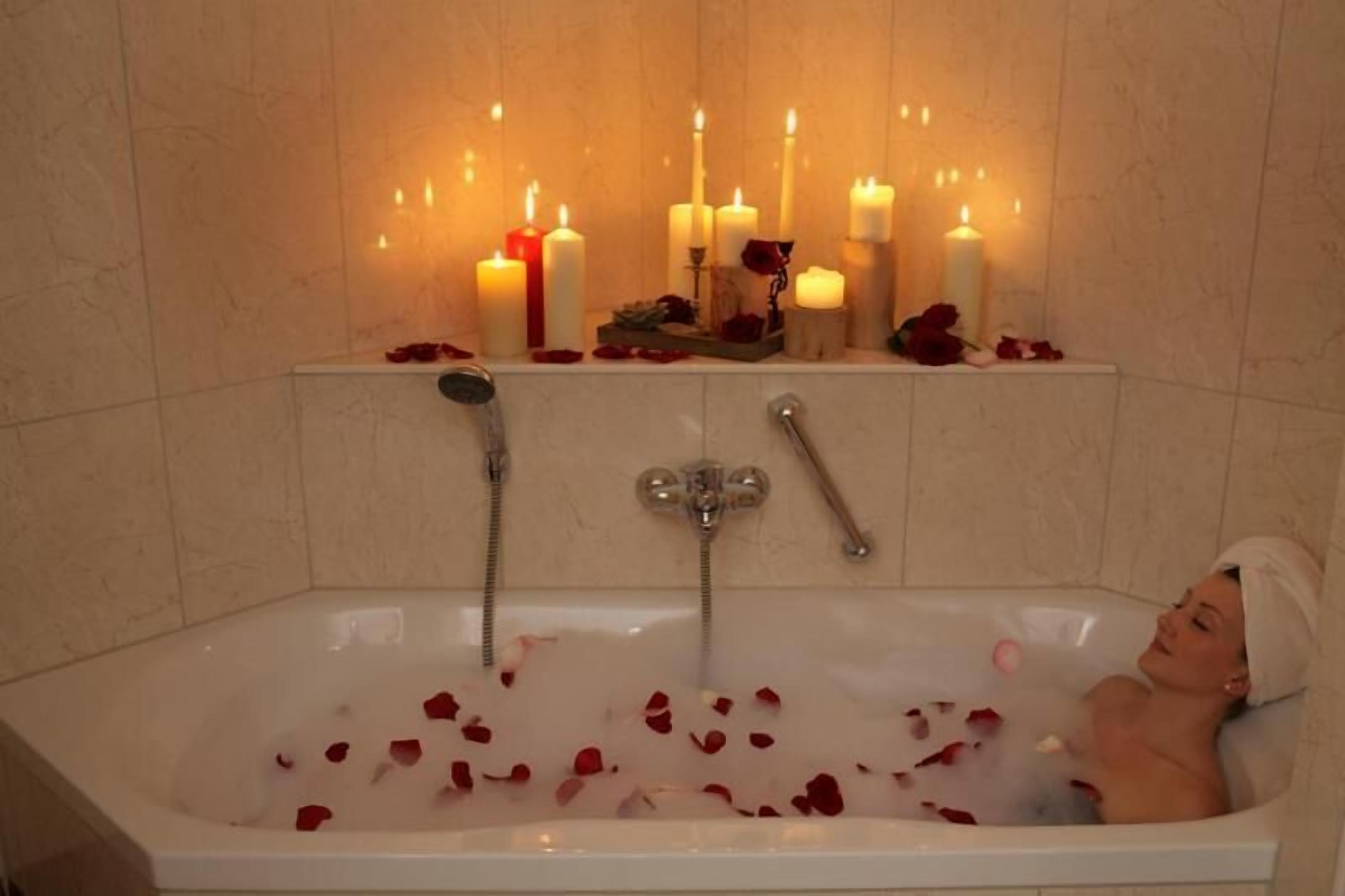 A bathtub with rose petals and candles.