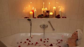 A bathtub with rose petals and candles.