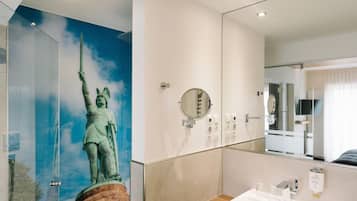 Un baño con un espejo grande, un lavamanos y una estatua de una mujer sosteniendo una espada.