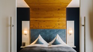 A modern bedroom with a large bed, wooden ceiling, and wall-mounted lights. - Germanenhof (Steinheim)