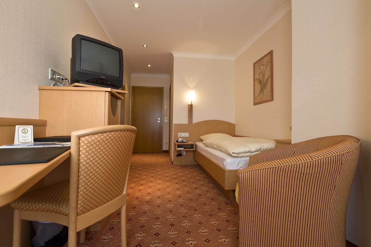 A hotel room with a bed, a desk, a chair, a television, a nightstand, and a lamp.