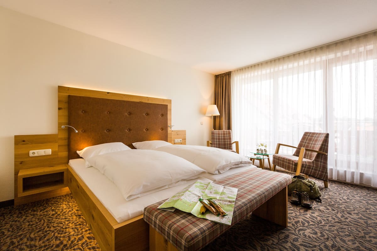 A hotel room with a large bed, a wooden nightstand, a chair, and a small table.