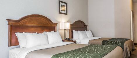 Habitación de hotel con dos camas, cabecero de madera, mesita de noche, lámpara y un cuadro en la pared.
