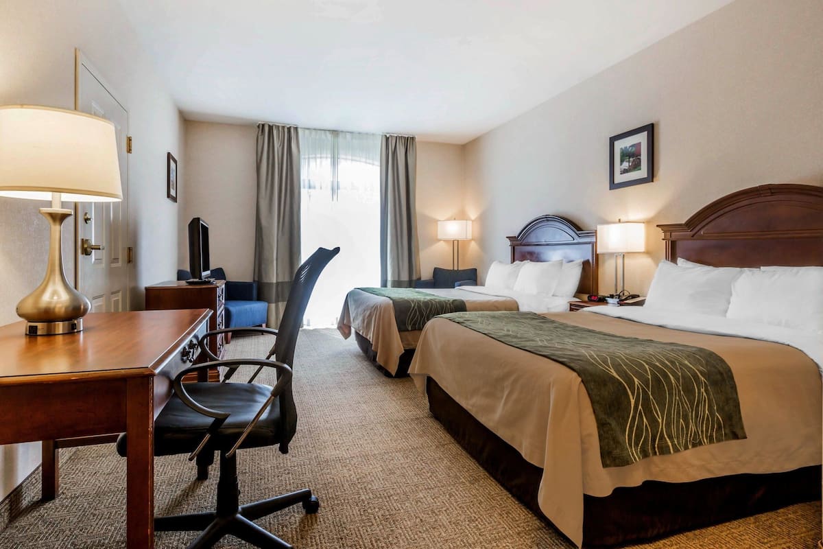 Ein Hotelzimmer mit zwei Betten, einem Schreibtisch mit Lampe, einem Sessel und einem Fernseher.