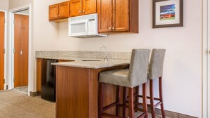 A kitchen with wooden cabinets, a microwave, a sink, and two bar stools. - Comfort Inn & Suites South Burlington near University (South Burlington)