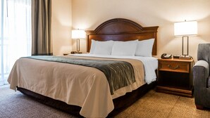 A neatly made bed with a wooden headboard, two bedside lamps, a nightstand with a telephone, and a chair. - Comfort Inn & Suites South Burlington near University (South Burlington)