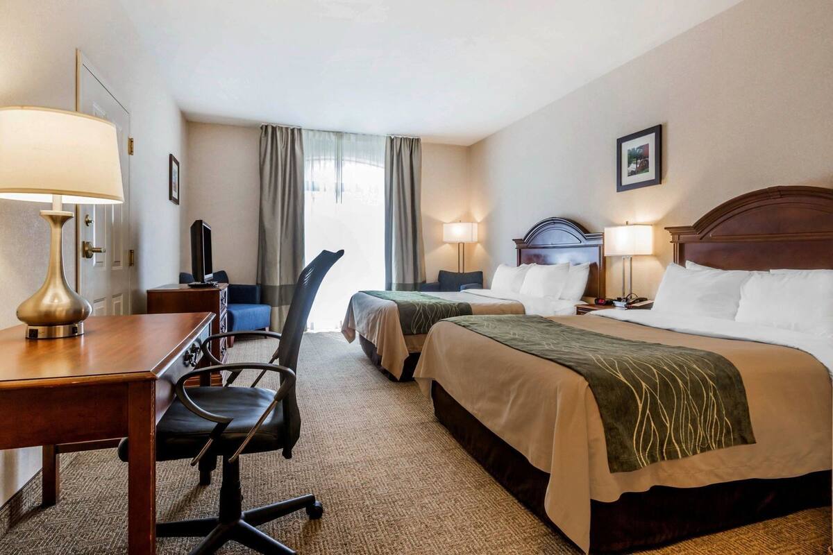 A hotel room with two beds, a desk with a lamp, a chair, and a television.