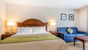 A hotel room with a large bed, two bedside tables with lamps, a blue sofa, a wooden coffee table, and two framed pictures on the wall.