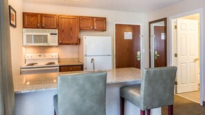 A kitchen with wooden cabinets, a microwave, stove, refrigerator, and bar stools. - Comfort Inn & Suites South Burlington near University (South Burlington)