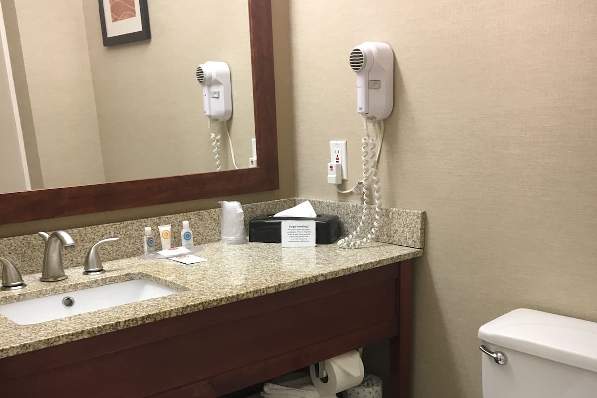 Ein Badezimmer mit Granitwaschtisch, Spiegel, Haartrockner, Toilette und Ablagefläche mit gefalteten Handtüchern.