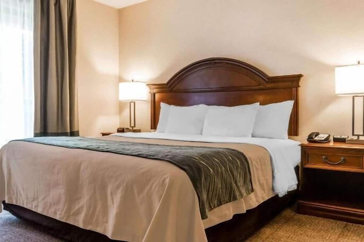 Ein Hotelzimmer mit einem großen Bett, zwei Nachttischen, einem Sessel und einer Lampe.