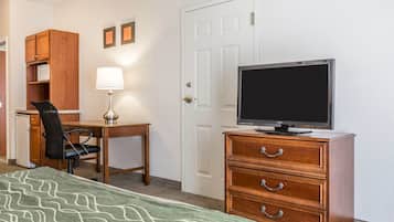 A hotel room with a bed, a desk with a chair, a television on a dresser, and a door.