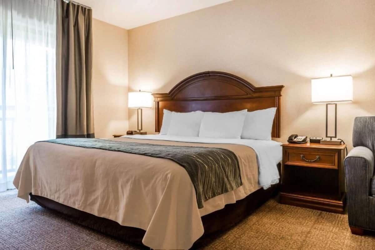 Ein Hotelzimmer mit einem großen Bett, zwei Nachttischlampen, einem Nachttisch mit Telefon und einem Sessel.