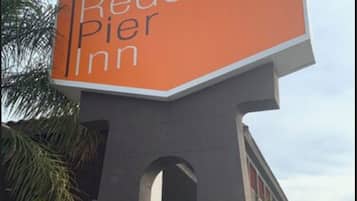 A Redondo Inn sign with a prominent 'R' logo, set against a modern building facade with palm trees and a clear sky.