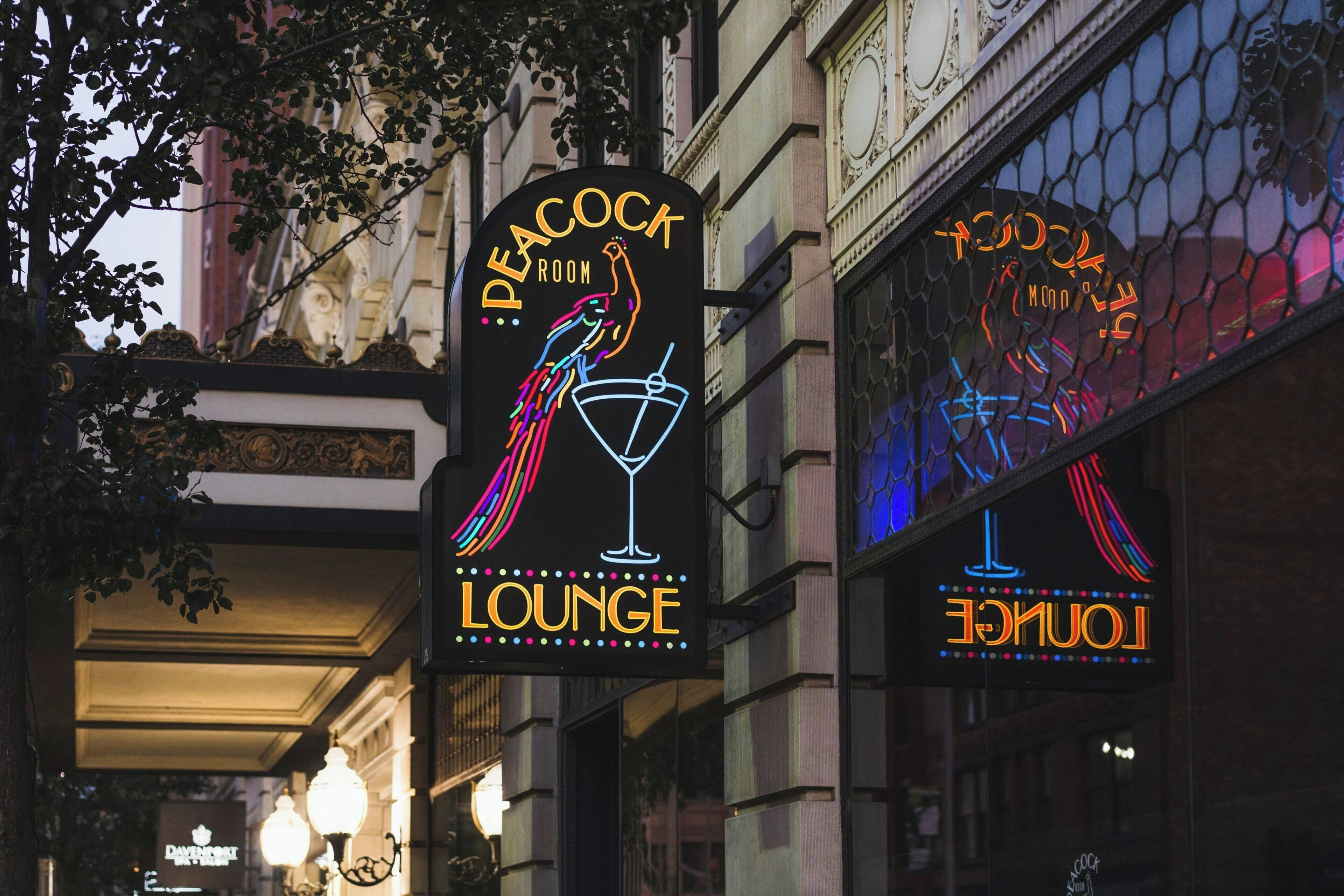 A neon sign for Peacock Lounge with a peacock and cocktail glass.