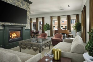 A living room with a fireplace, seating area, piano, and large windows. - Davenport Hotel, Autograph Collection (Spokane)