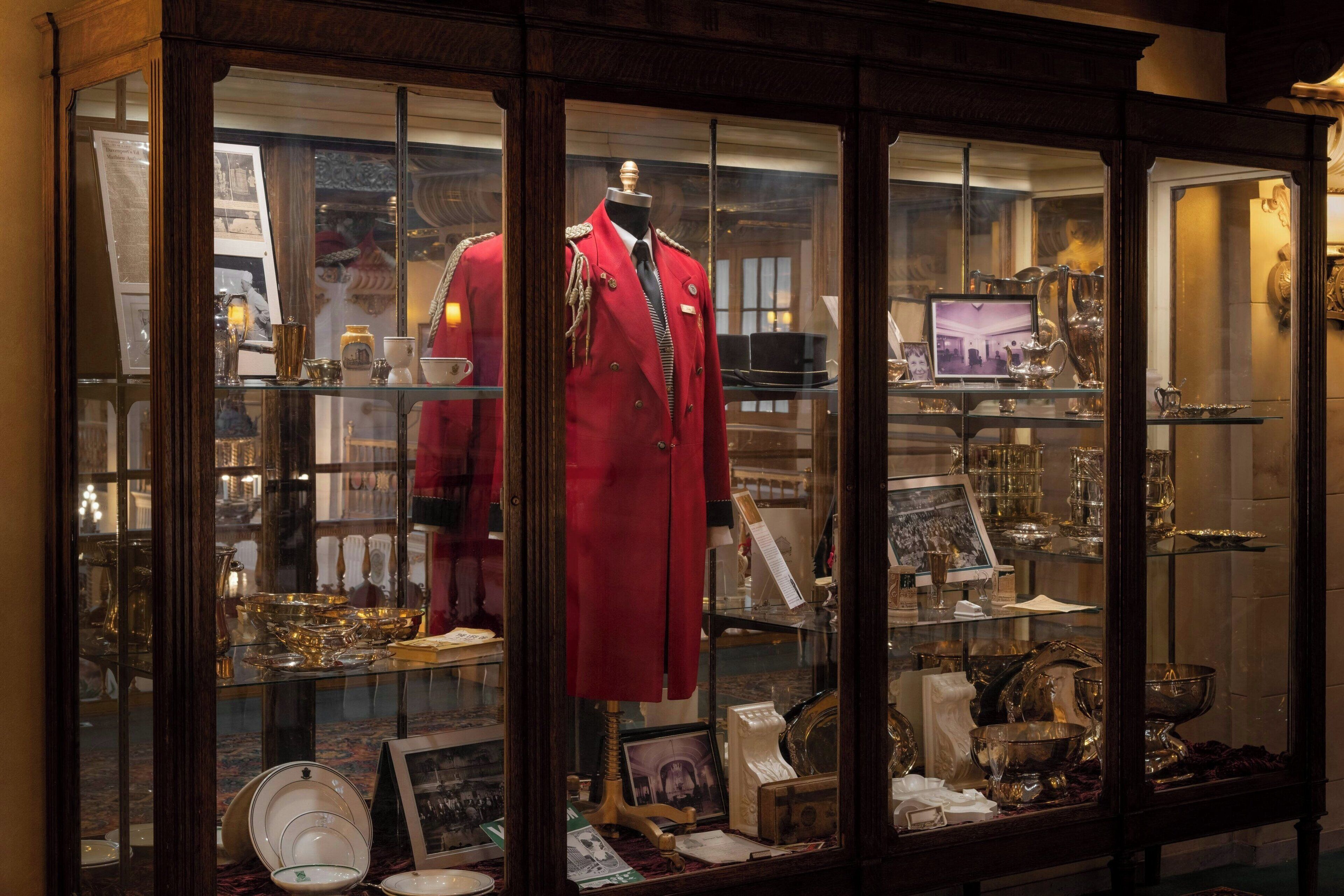 A display case with a mannequin in a red coat, various glassware, and framed photographs.