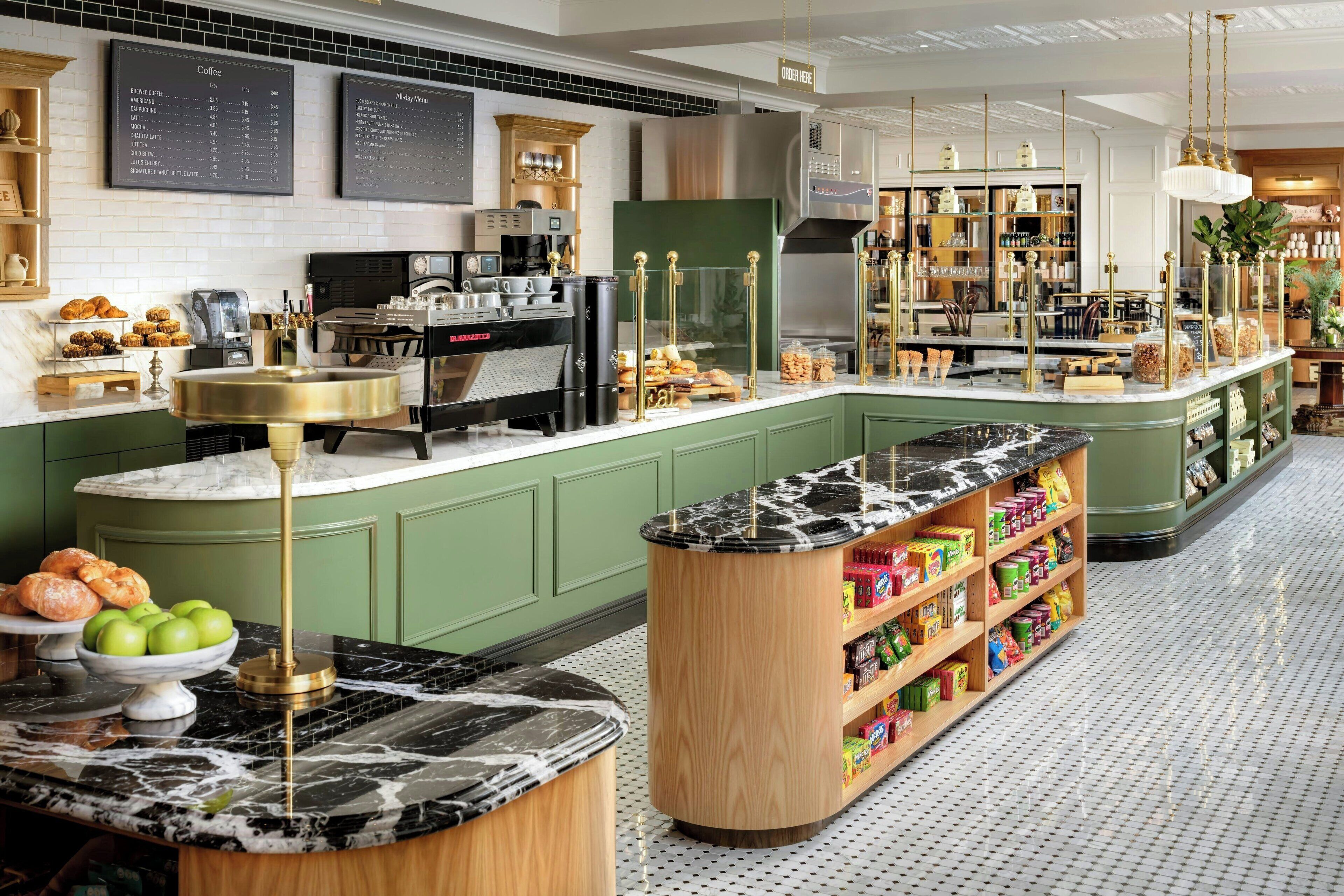 A modern cafe with a marble counter, green cabinets, and a variety of food items displayed.