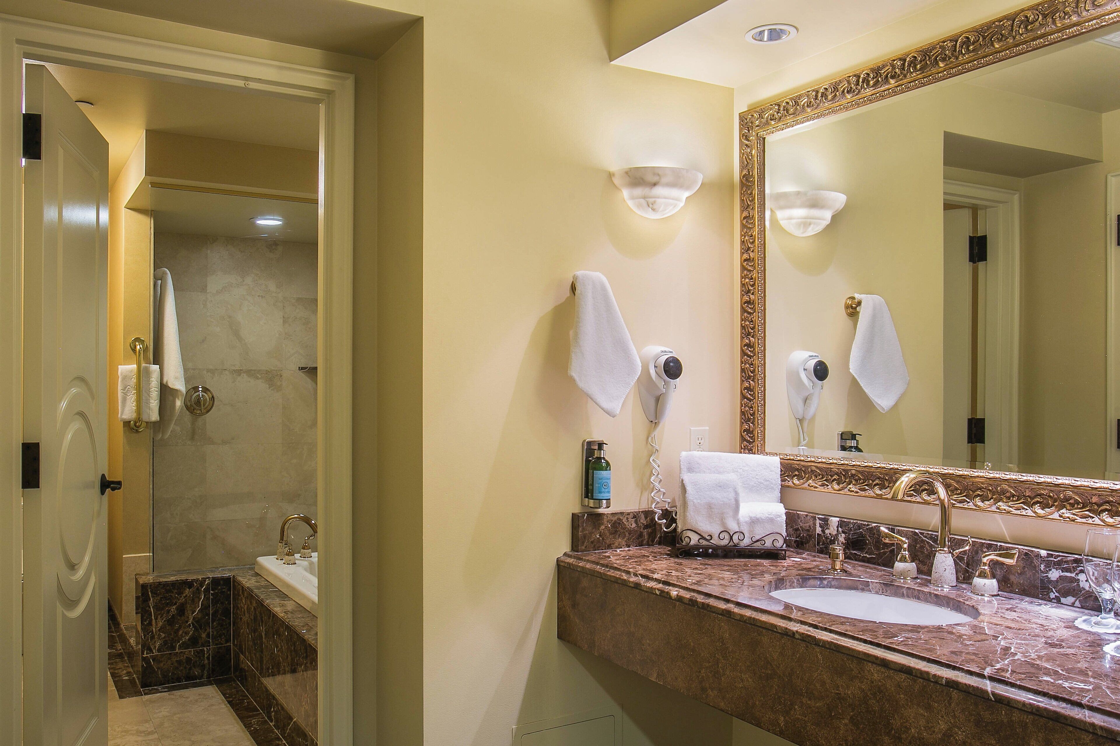 A bathroom with a marble sink, a large mirror, and a hairdryer on the wall.