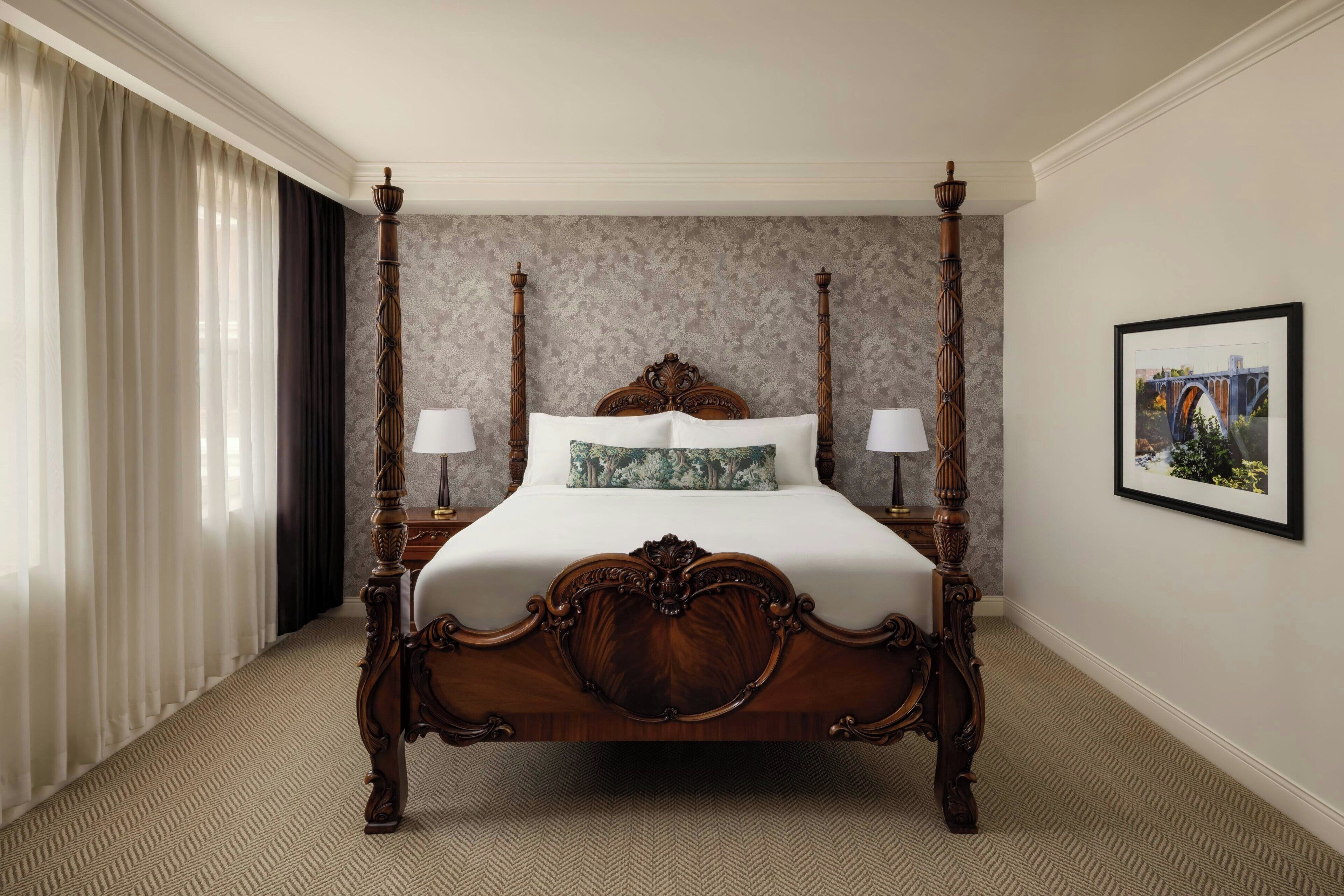 A four-poster bed with ornate woodwork, a patterned wall, and a framed picture on the wall.