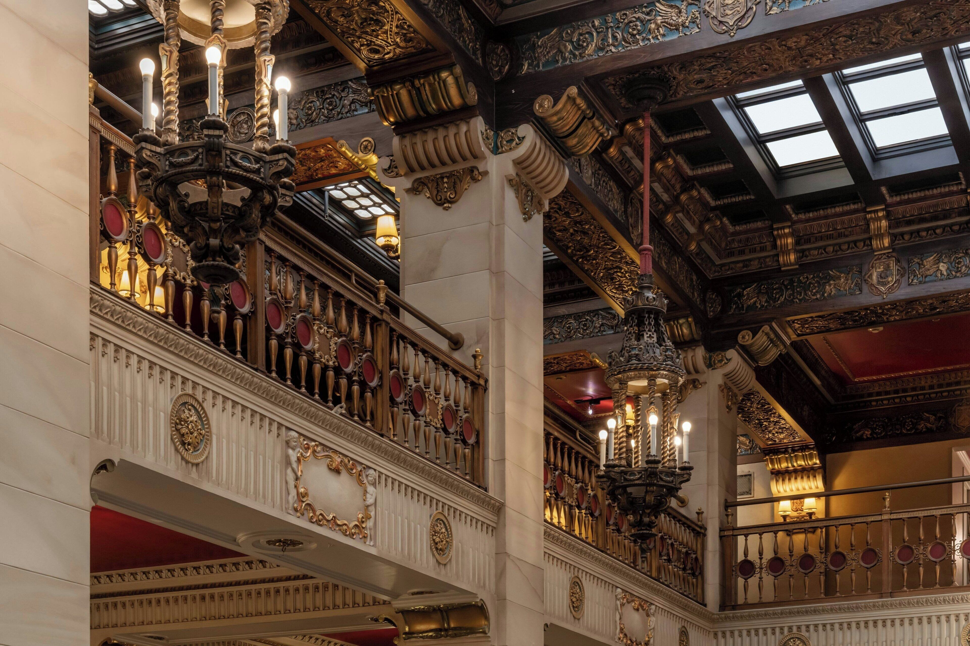 An ornate interior with a grand staircase, chandeliers, and detailed ceiling artwork.