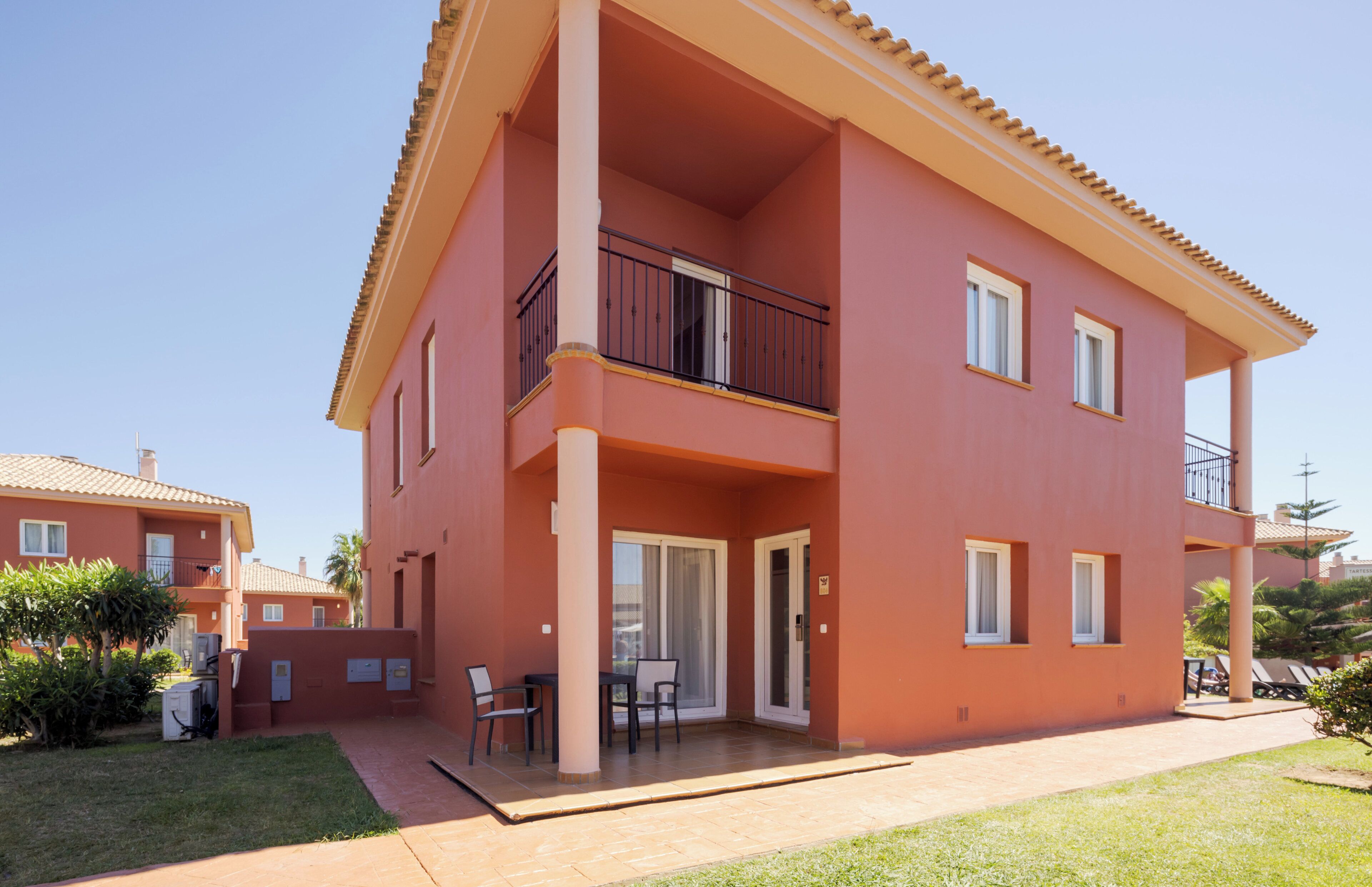 A two-story building with a balcony, a patio with chairs, and a small garden area.