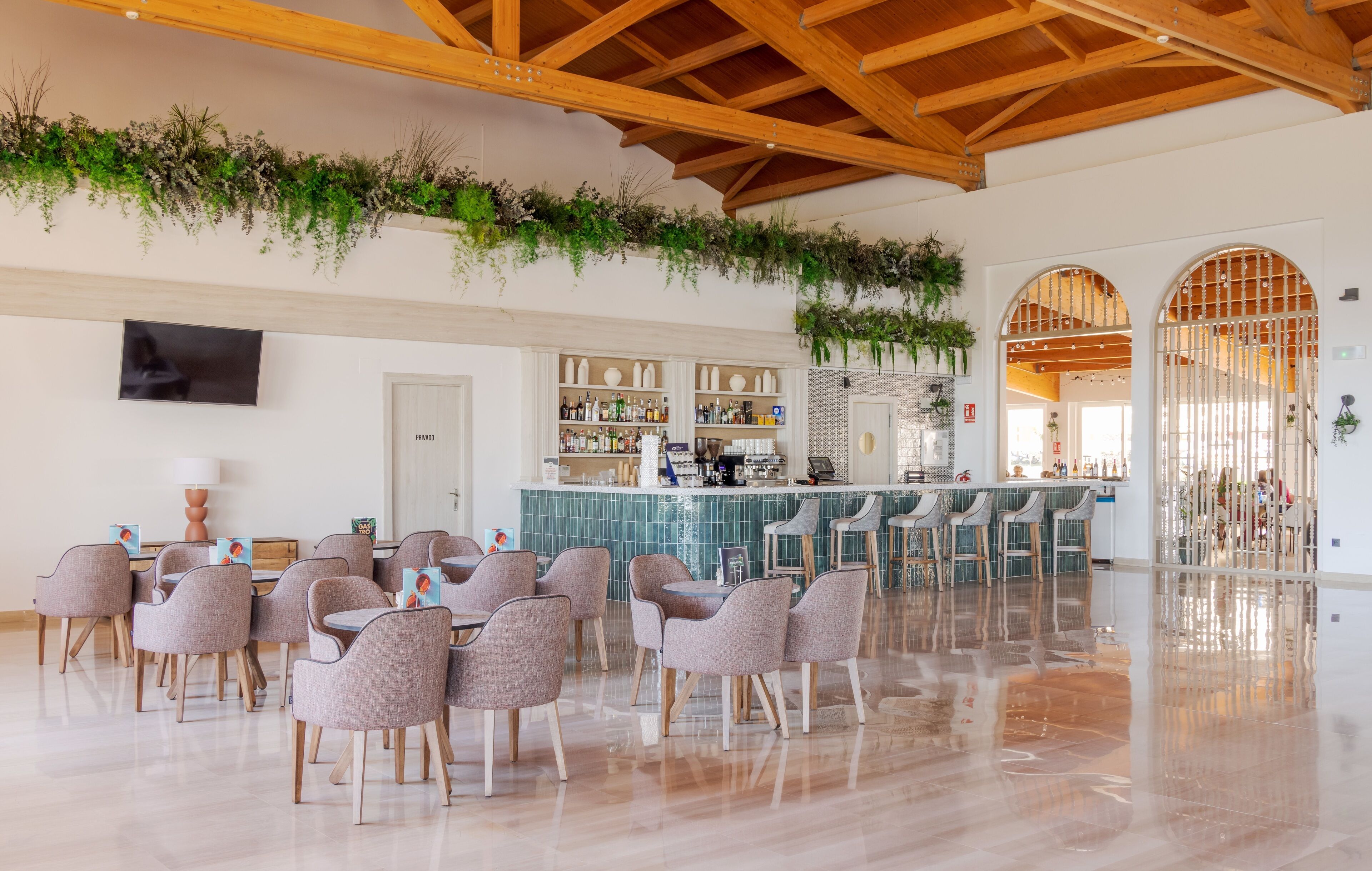 A spacious dining area with a bar, wooden ceiling beams, and green plants on the walls.