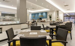 A modern restaurant with a central bar, dining tables with chairs, and a blue accent wall. - Aparthotel ILUNION Sancti Petri (Chiclana de la Frontera)