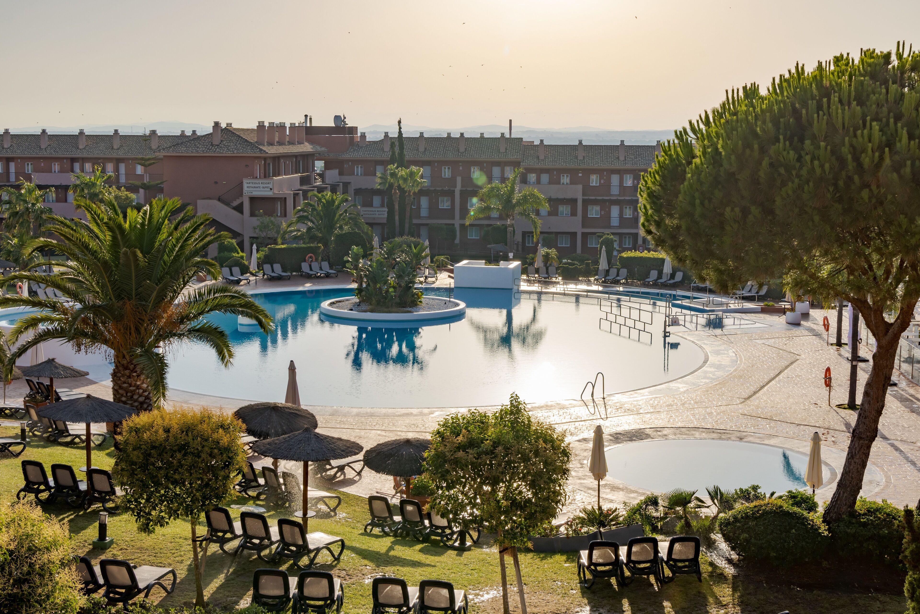 A resort pool area with lounge chairs, umbrellas, and a large central pool.