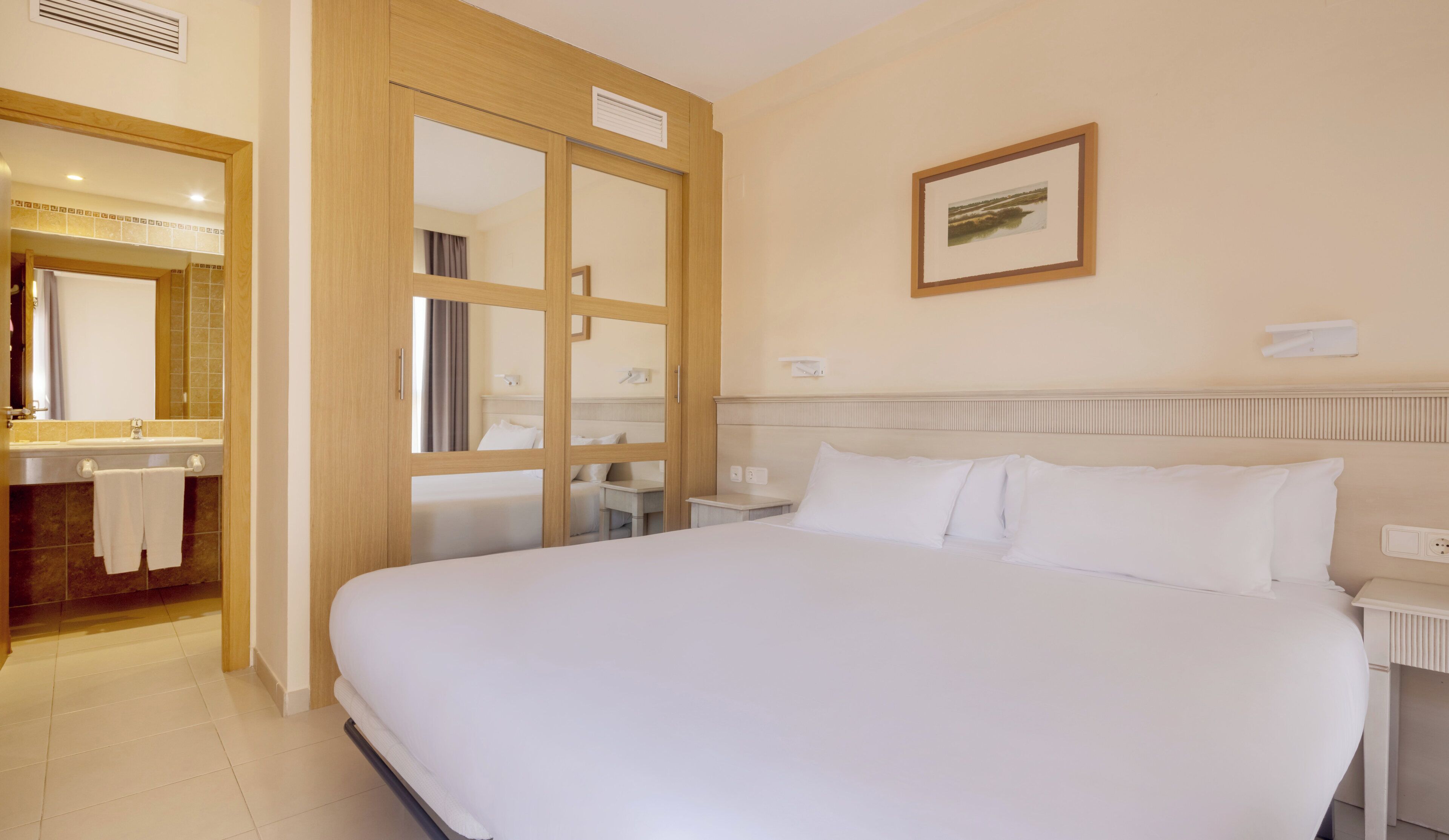 Ein Hotelzimmer mit einem großen Bett, einem Badezimmer mit Spiegel und Waschbecken sowie einem gerahmten Bild an der Wand.