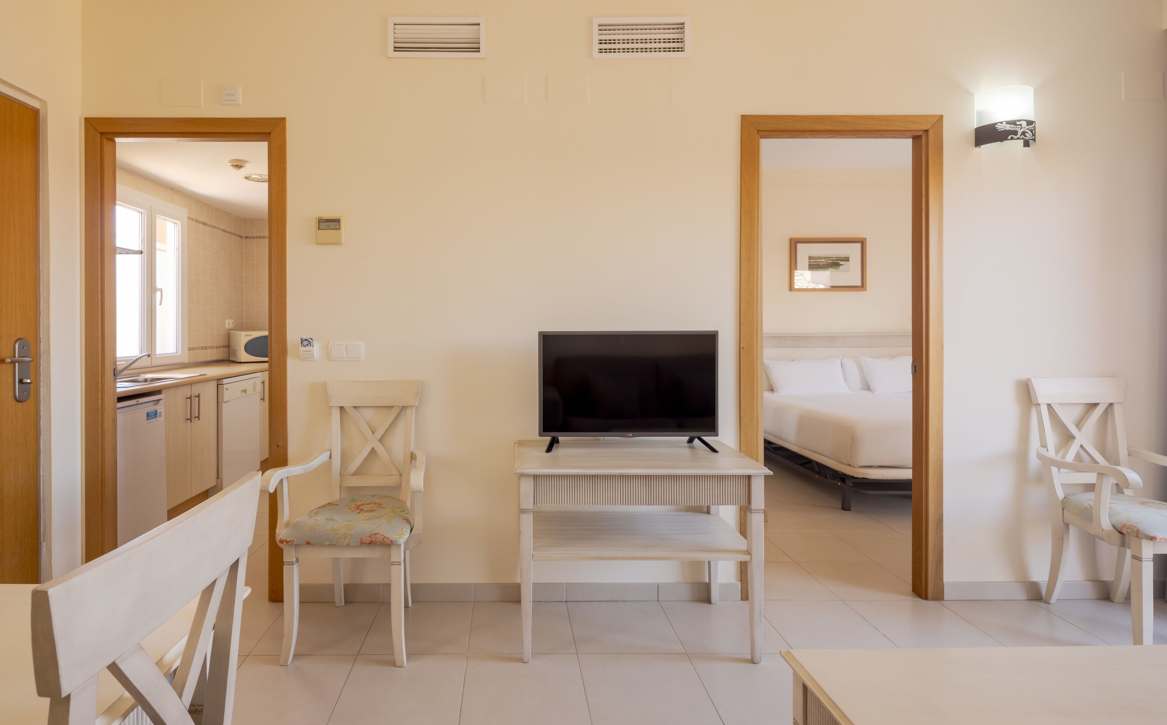 A hotel room with a TV on a stand, a bed, a chair, and a small table.
