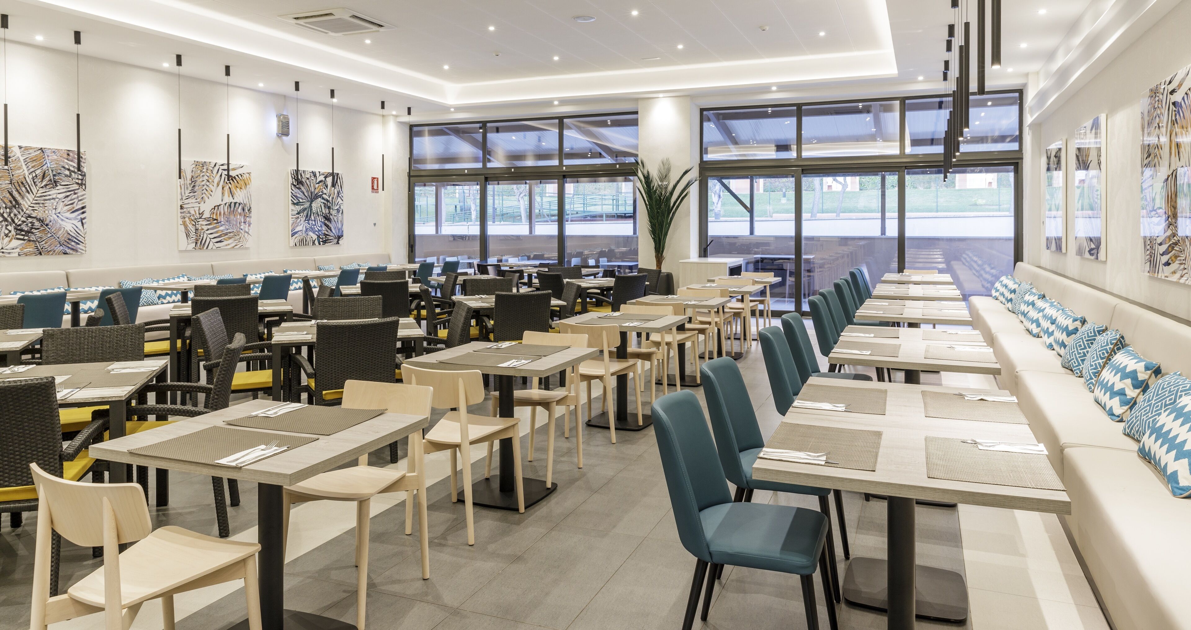 A modern dining area with long tables and chairs, large windows, and abstract art on the walls.