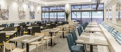 A modern dining area with long tables and chairs, large windows, and abstract art on the walls.