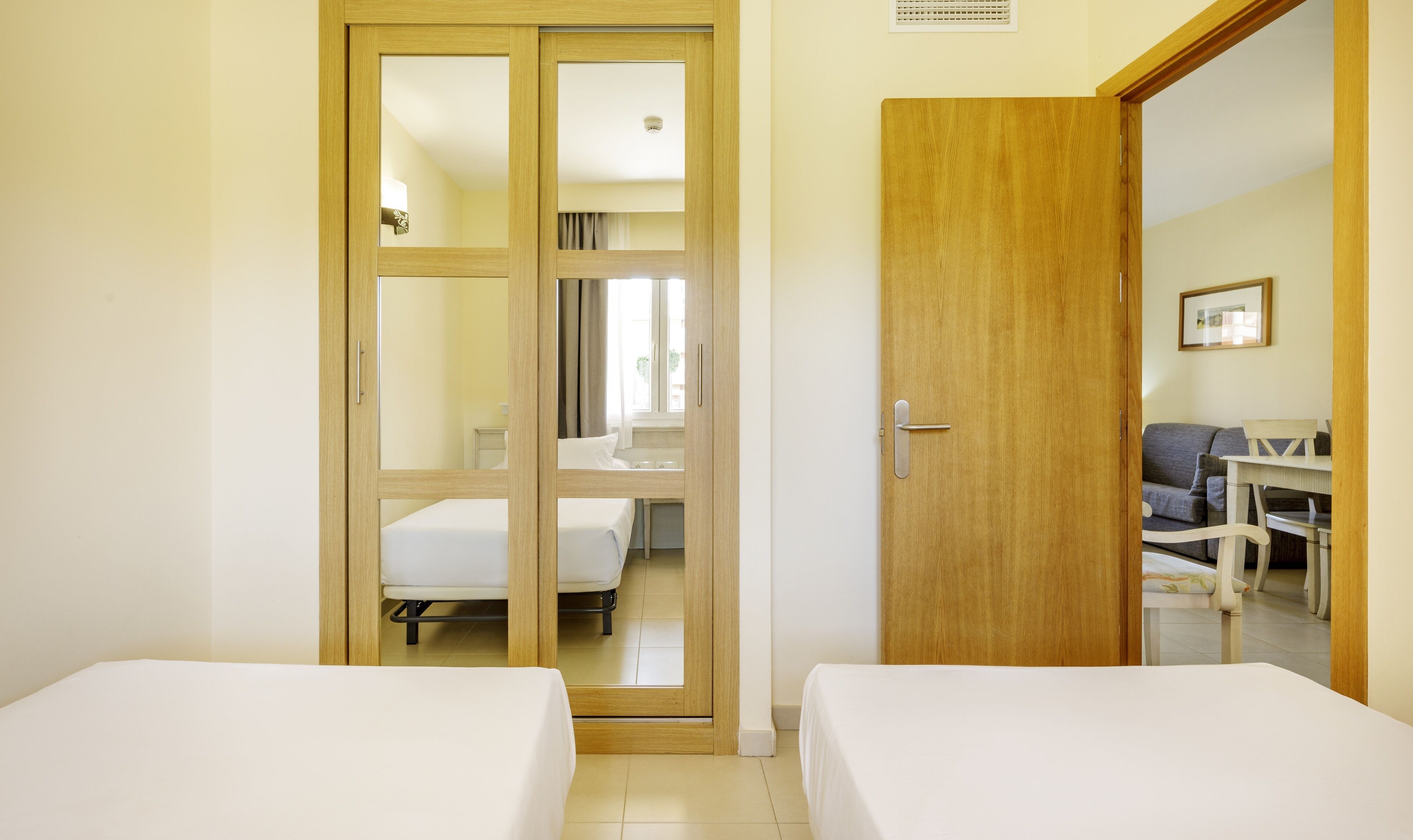 A hotel room with two single beds, a wooden door, a small table with chairs, and a sofa.