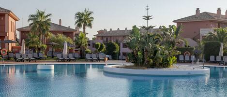 A swimming pool with lounge chairs and palm trees, surrounded by resort buildings.