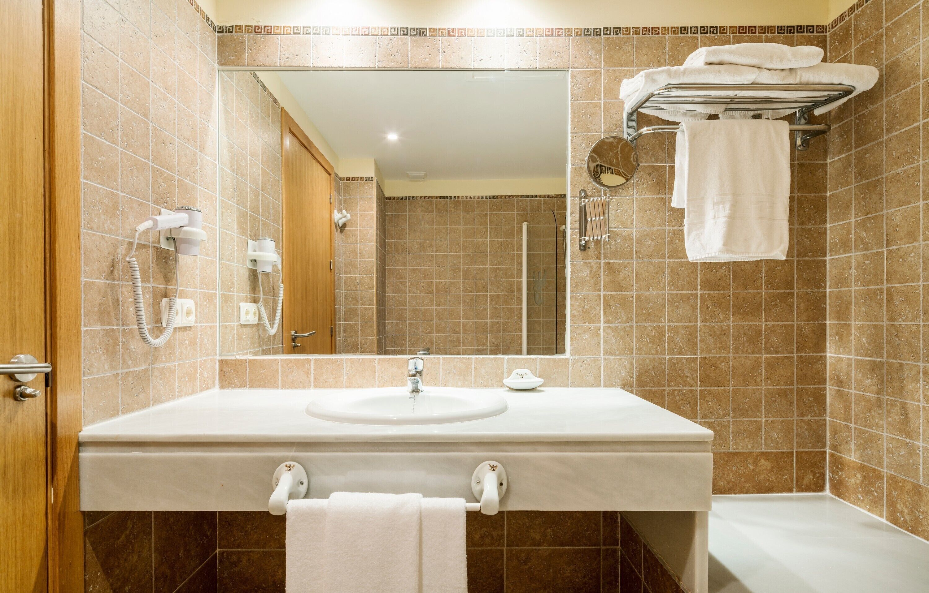Un baño con lavamanos, espejo, toallero y ducha.