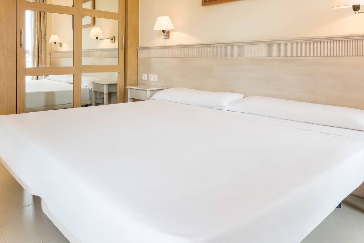 Une chambre d’hôtel avec un grand lit, une armoire en bois et une salle de bain équipée d’un miroir et d’un porte-serviettes.