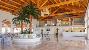 A spacious lobby with a high wooden ceiling, a central seating area with a palm tree, and a reception desk on the right.