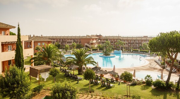 A hotel with a large swimming pool surrounded by lounge chairs and palm trees. - Aparthotel ILUNION Sancti Petri (Chiclana de la Frontera)