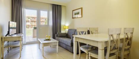 A furnished living room with a sofa, a dining table with chairs, a TV, and a window with curtains.