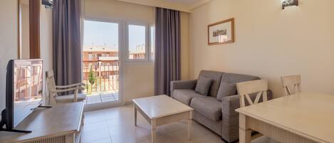 A living room with a sofa, a table, a TV, and a balcony with curtains.