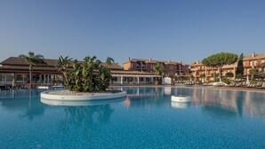 A large swimming pool with a circular island, surrounded by buildings with balconies and palm trees.